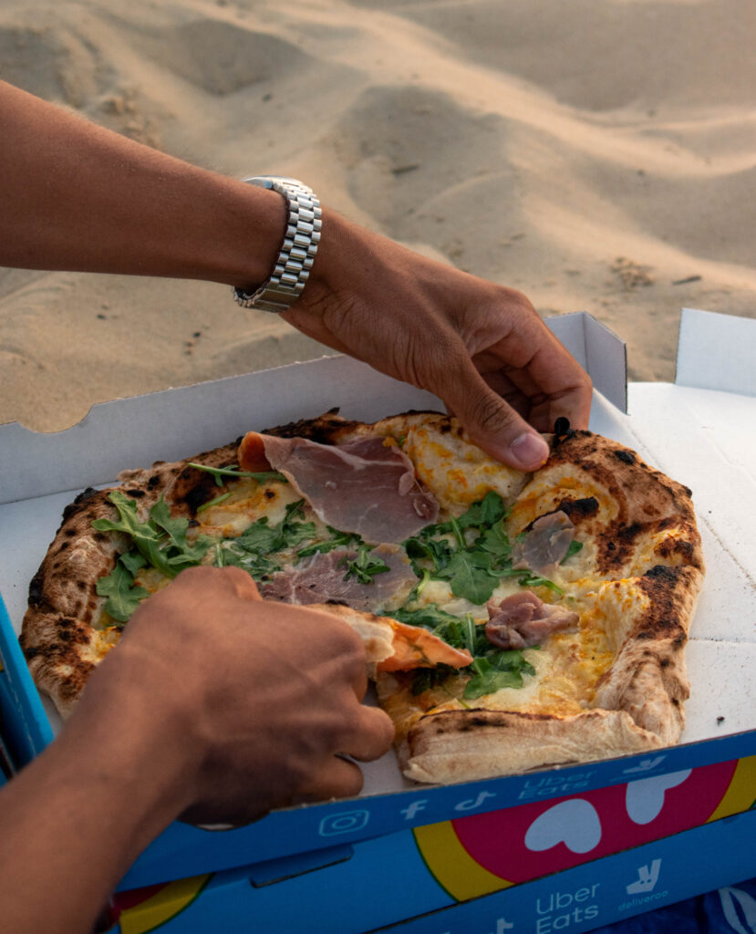 Livreur tenant une pizza napolitaine fumante devant une porte à Bruges