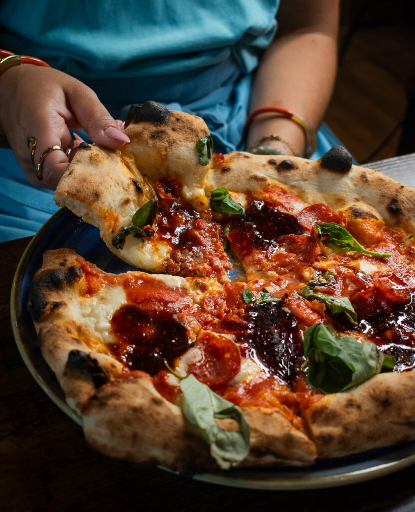 Pizzaiolo étirant une pâte, ingrédients frais et four à bois en arrière-plan