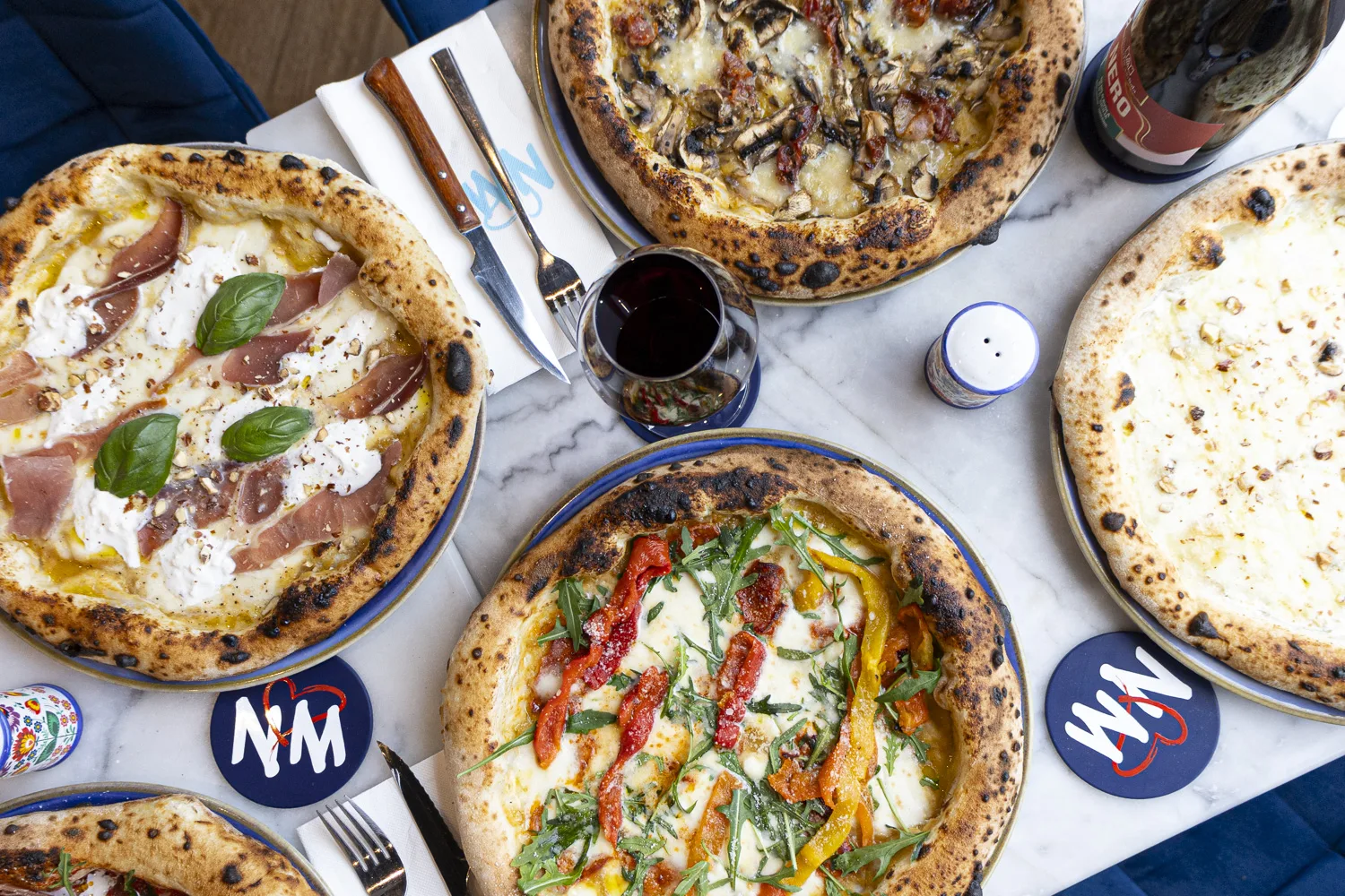 Pizzaïolo étire la pâte, ingrédients San Marzano, basilic, four à bois en fond