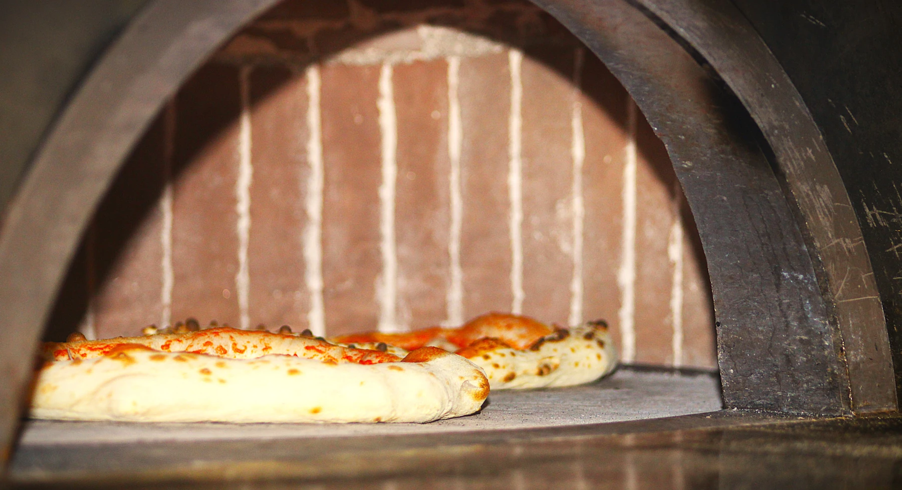 Pizzas napolitaines cuisant côte à côte dans un four à bois traditionnel.