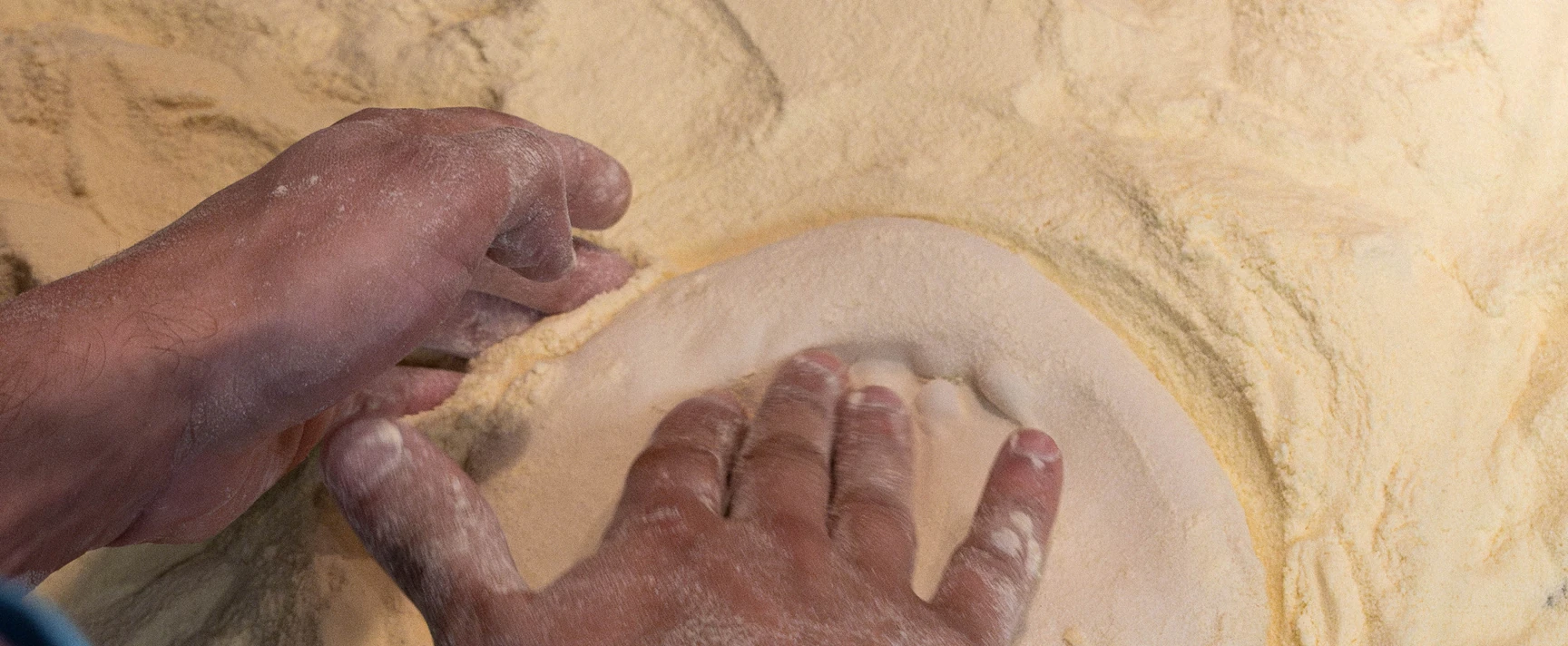 Mains de pizzaiolo façonnant un pâton de pâte dans la farine tipo 00.