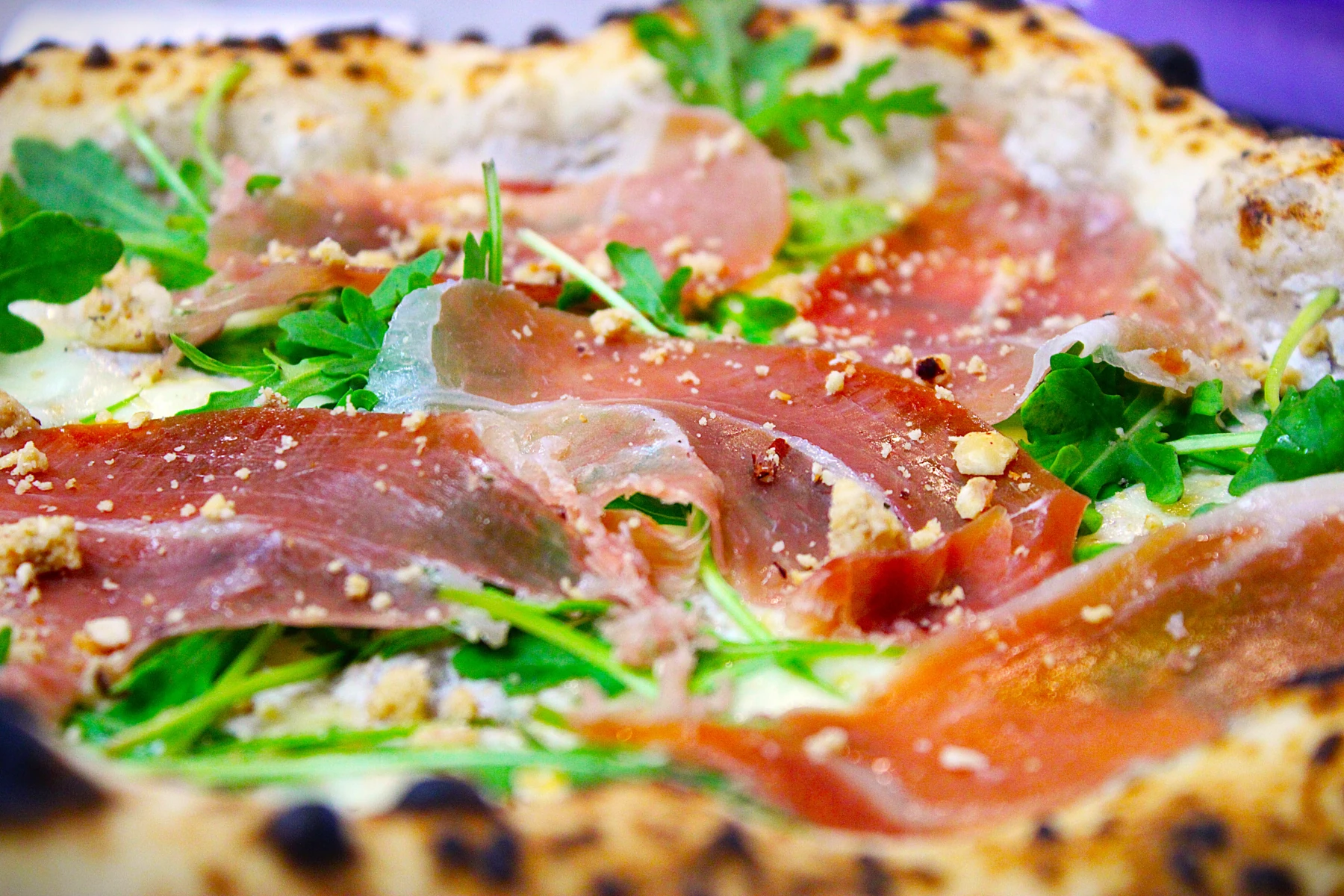 Pizza napolitaine garnie de jambon cru, roquette et copeaux de fromage.