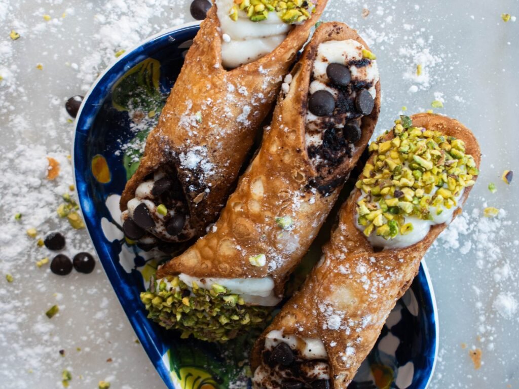 Cannoli de Nennella Mia saupoudrés de sucre glace dans un plat en céramique bleue