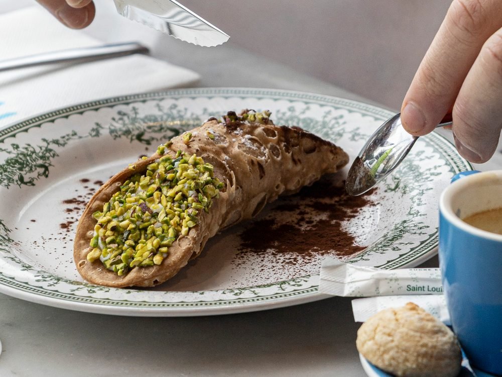 Cannolo à la pistache dégusté avec un café sur une table de Nennella Mia