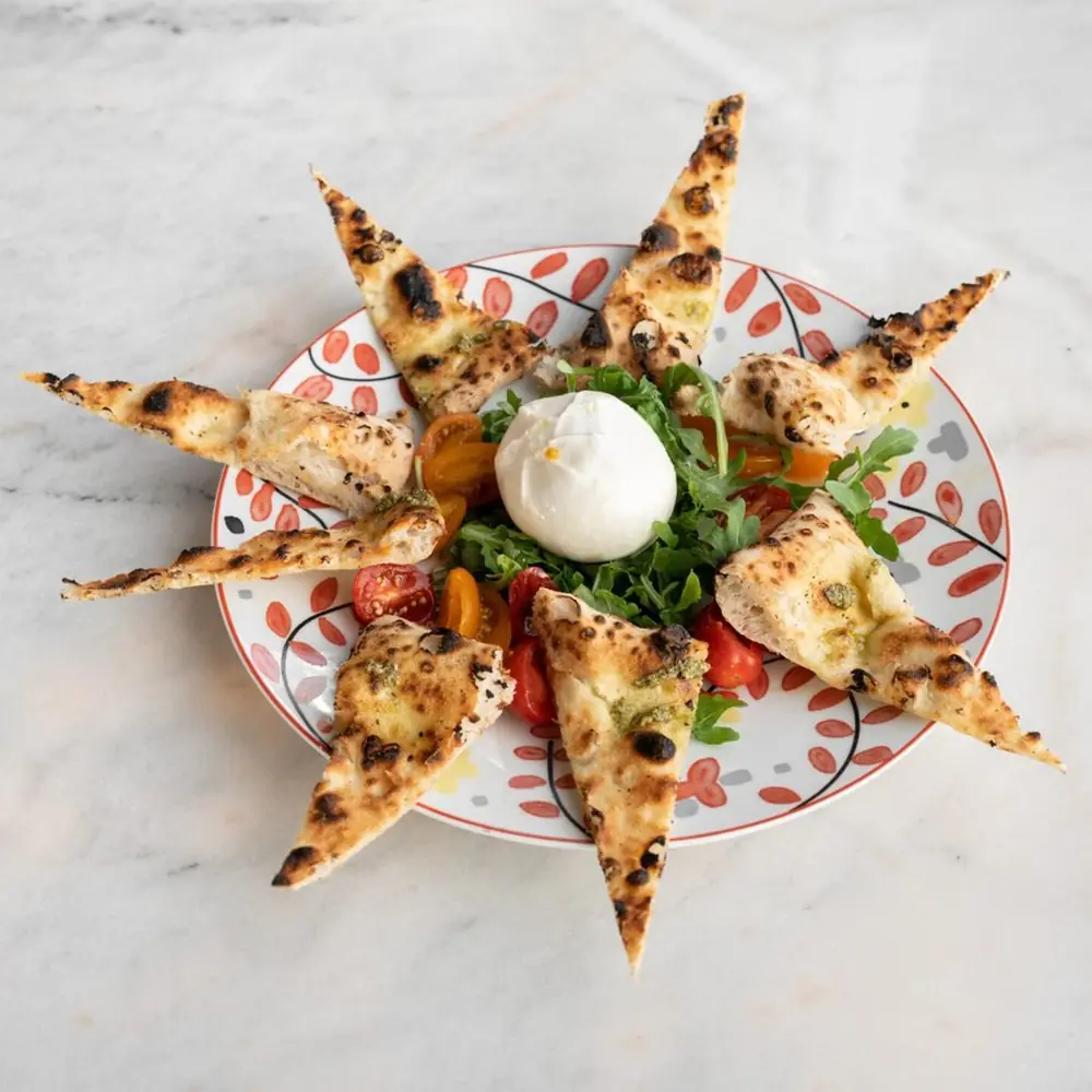 Burrata Mia Caprese entourée de triangles de pâte cuite au four, sur une assiette de Nennella Mia