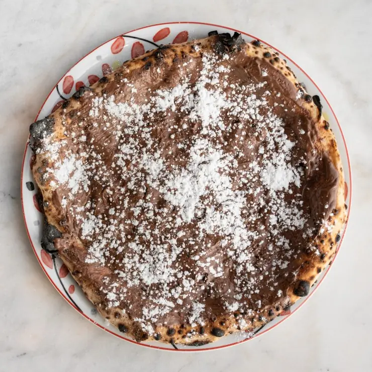 Pizza Nutella saupoudrée de sucre glace, vue du dessus sur une table en marbre de Nennella Mia