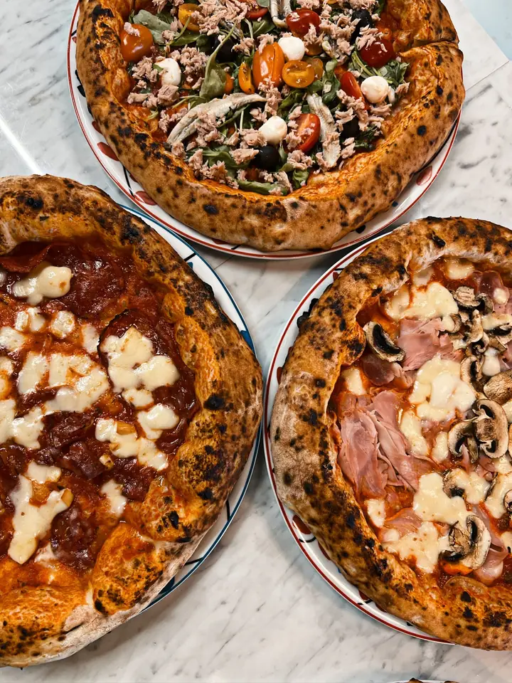 Trois pizzas napolitaines de Nennella Mia vues du dessus sur une table en marbre