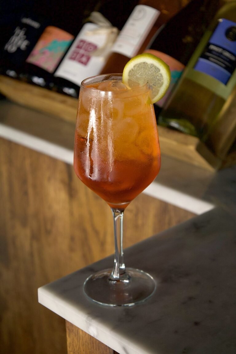 Aperol Spritz orange dans un verre à pied avec glaçons et rondelle de citron, sur le bar en marbre de Nennella Mia