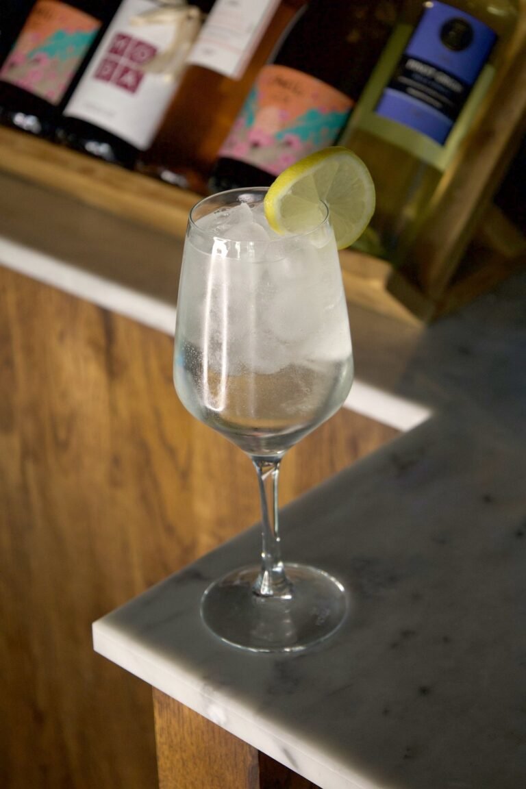 Basilico Spritz clair dans un verre à pied avec glaçons et rondelle de citron, sur le bar en marbre de Nennella Mia