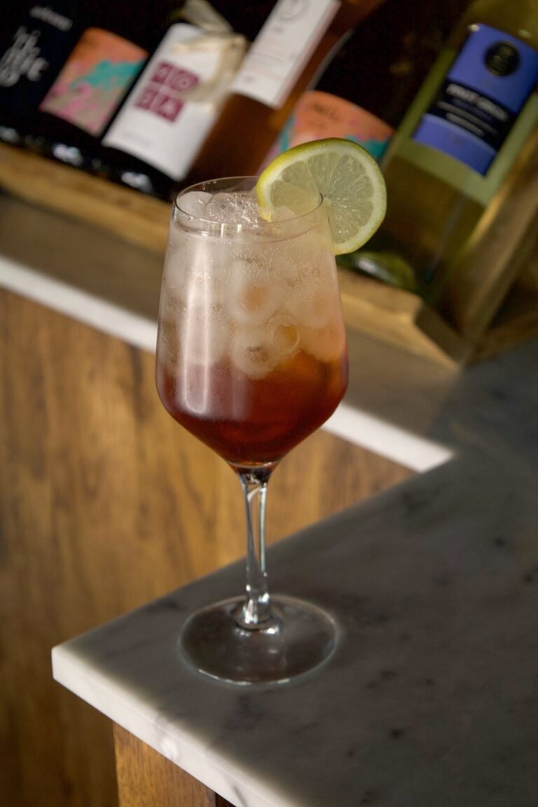 Bouscat Americano rouge dans un verre à pied avec glaçons et rondelle de citron, sur le bar en marbre de Nennella Mia