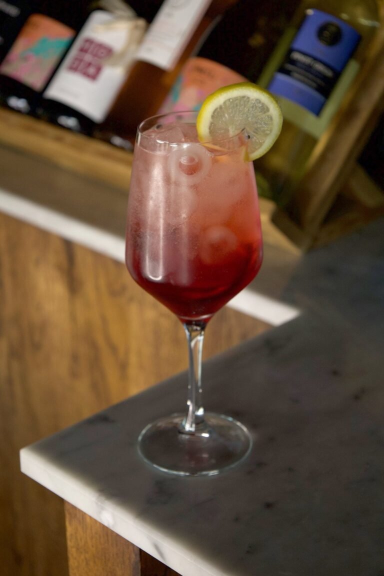 Campari Spritz rouge dans un verre à pied avec glaçons et rondelle de citron, sur le bar en marbre de Nennella Mia