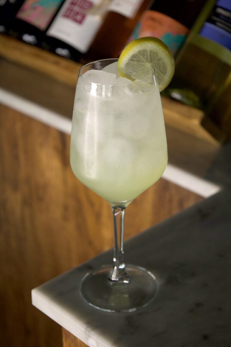 Capri Diem vert pâle dans un verre à pied avec glaçons et rondelle de citron, sur le bar en marbre de Nennella Mia