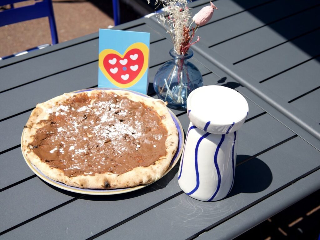 Pizza Nutella sur une table de la terrasse de Nennella Mia, à côté d'un vase blanc rayé de bleu