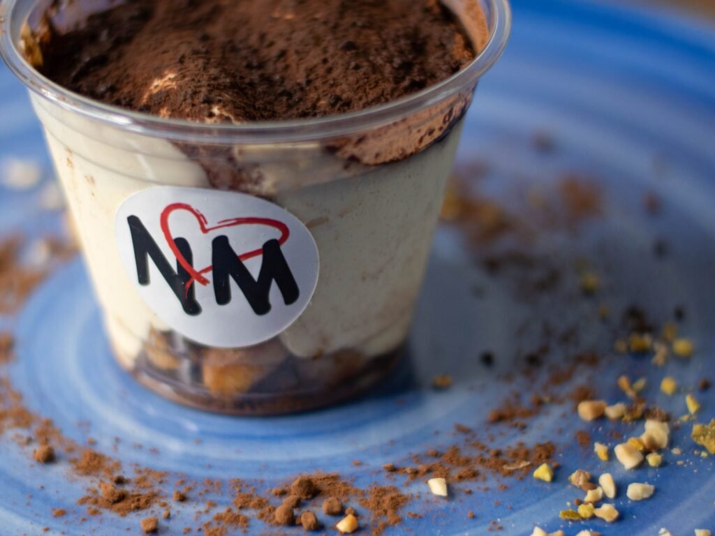 Tiramisù maison de Nennella Mia dans son pot, saupoudré de cacao, sur une assiette bleue